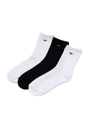 Trzy skarpetki do kostki, dwie białe i jedna czarna, każda z małym czerwonym sercem blisko górnej krawędzi, ułożone obok siebie.