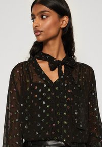Schwarze durchsichtige Bluse mit Kragen, verziert mit bunten Paillettenmustern, langen Ärmeln und einer gebundenen Schleifendetail am Kragen.