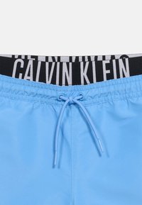 Ανοιχτό μπλε ανδρικό μαγιό με μπροστινό κορδόνι δεμένο σε κόμπο και μαύρη μέση με λευκή σήμανση Calvin Klein.