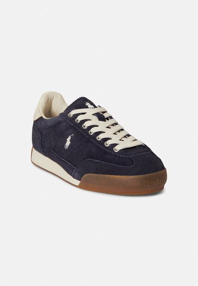 Νάυλον σουέντ αθλητικό παπούτσι σε ναυτικό μπλε με κρεμ κορδόνια, λαστιχένια σόλα και κεντημένο λογότυπο στο πλάι. Διαθέτει στρογγυλεμένη μύτη και υφή στην πάνω επιφάνεια.