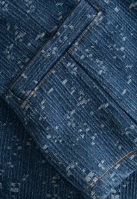 Tessuto denim con un motivo testurizzato in filo blu scuro e blu chiaro. Presenta una tasca visibile e cuciture arancioni a contrasto.