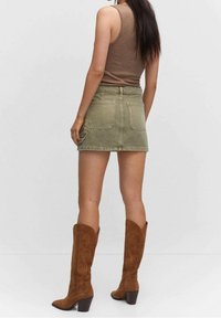 Olijfgroen denim rok met twee achterzakken; gecombineerd met een bruine tanktop en bruine suède kniehoge laarzen met een blokhak.