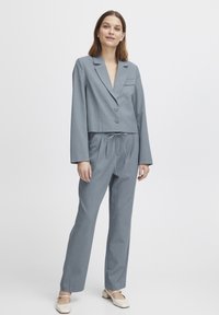 Helles blaues, tailliertes Blazer mit zwei Knöpfen, passende Jogginghose mit Kordelzug, glattes Material und minimalistisches Design. Getragen mit cremefarbenen Ballerinas.