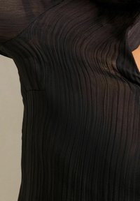 Black pleated garment featuring a lightweight, sheer fabric with vertical ripples, highlighting a textured surface and a fitted silhouette.
