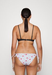 Top de bikini preto com alças ajustáveis e fecho nas costas, combinado com partes de baixo cinza claro com um pequeno padrão floral e laços laterais.