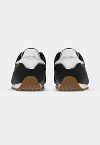 Ténis atléticos pretos e brancos com acabamento em couro liso, sola de borracha e padrão de tração texturizado. Logótipo "Karl Lagerfeld" no calcanhar.