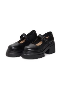 Pantofi Mary Jane din piele neagră, cu vârf rotund, curea ajustabilă, talpă groasă și finisaj texturat. Potriviți pentru diverse ocazii.