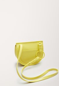Borsa a tracolla gialla realizzata in materiale liscio, con design curvo, tracolla regolabile e tasca frontale con dettaglio hardware circolare.