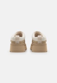 Beige zamšādas apavi ar baltiem ādas akcentiem un mīkstu iekšpusi. Iezīmējas ar biezu beige krāsas zoli un cilpu pie papēža vieglai uzvilkšanai.