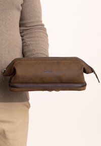 Pochette con zip in pelle marrone dal texture liscia, con logo impresso sul lato e una zip in contrasto di un marrone scuro.