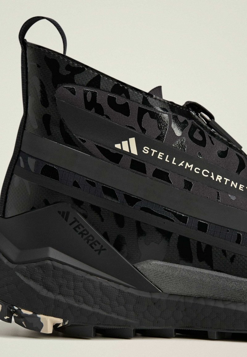 Zwarte sneaker met een luipaardprintpatroon, voorzien van een textuurmateriaal, rubberen zool en merknamen van Stella McCartney en Terrex.