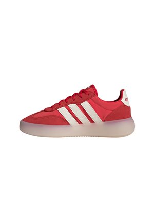 Sneaker bassa rossa con strisce bianche, lacci rossi e suola traslucida, mostrata di lato su sfondo bianco.