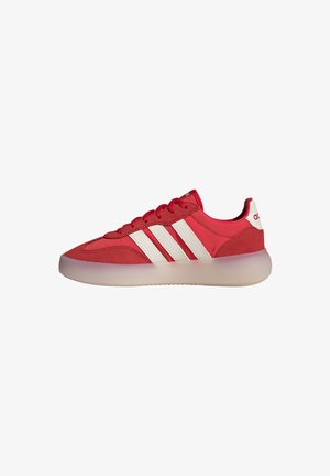 Zapatilla deportiva roja de corte bajo con rayas blancas, cordones rojos y suela translúcida, vista de lado sobre un fondo blanco.