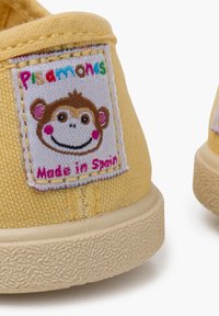 Gele canvas schoenen met een gestructureerd oppervlak, rubberen zool en een gestikt etiket met een aapgrafiek en de tekst "Made in Spain".
