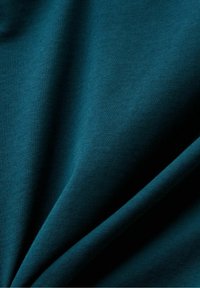 Tealfärgad tyg med en slät textur, som har en subtil elastisk stretch, faller med mjuka veck och visar en jämn, enhetlig färg.