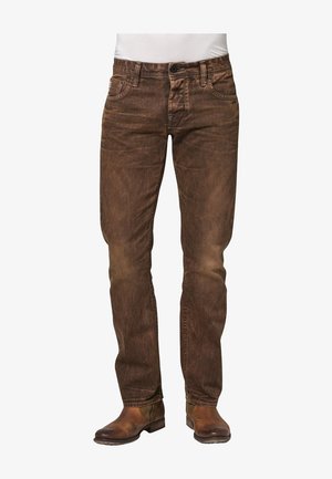 Jeans de denim marrón con un acabado desgastado, diseño de cinco bolsillos y corte recto. Usados con botas de cuero marrón.