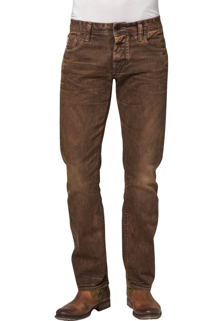 Jeans de denim marrón con un acabado desgastado, diseño de cinco bolsillos y corte recto. Usados con botas de cuero marrón.
