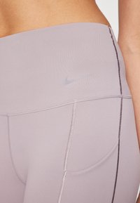 Leggings lilas clair avec une texture lisse, dotés d'un logo Nike ton sur ton et de coutures contrastantes sur les côtés. Conçus avec des poches.