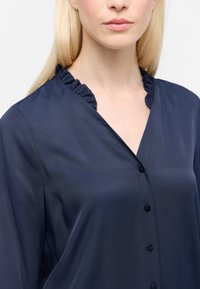 Camicia button-up blu navy con un sottile lucido, caratterizzata da un colletto arricciato e una superficie liscia. I bottoni sono scuri e si abbinano al tessuto.