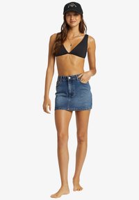 Černý bikiny top, denimová minisukně, ležérní póza. Sukně má přední zapínání na knoflíky, mírný třásně na spodním lemu. Kšiltovka dodává sportovní akcent.