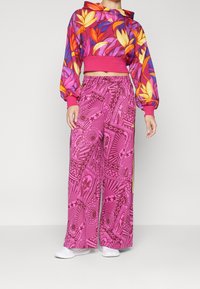 Färggad cropped hoodie med blommönster och rosa ärmar, matchad med vida rosa byxor med intrikata mönster och elastisk midja.