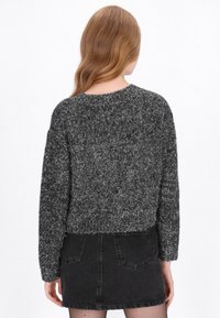 Zkrácený svetr v černé a šedé pletenině, s dlouhými rukávy, kulatým výstřihem a texturovaným povrchem. V kombinaci s černou džínsovou mini sukní.