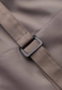 Gros plan d'une ceinture en tissu gris avec des coutures détaillées passée dans une boucle rectangulaire noire sur un vêtement gris lisse.
