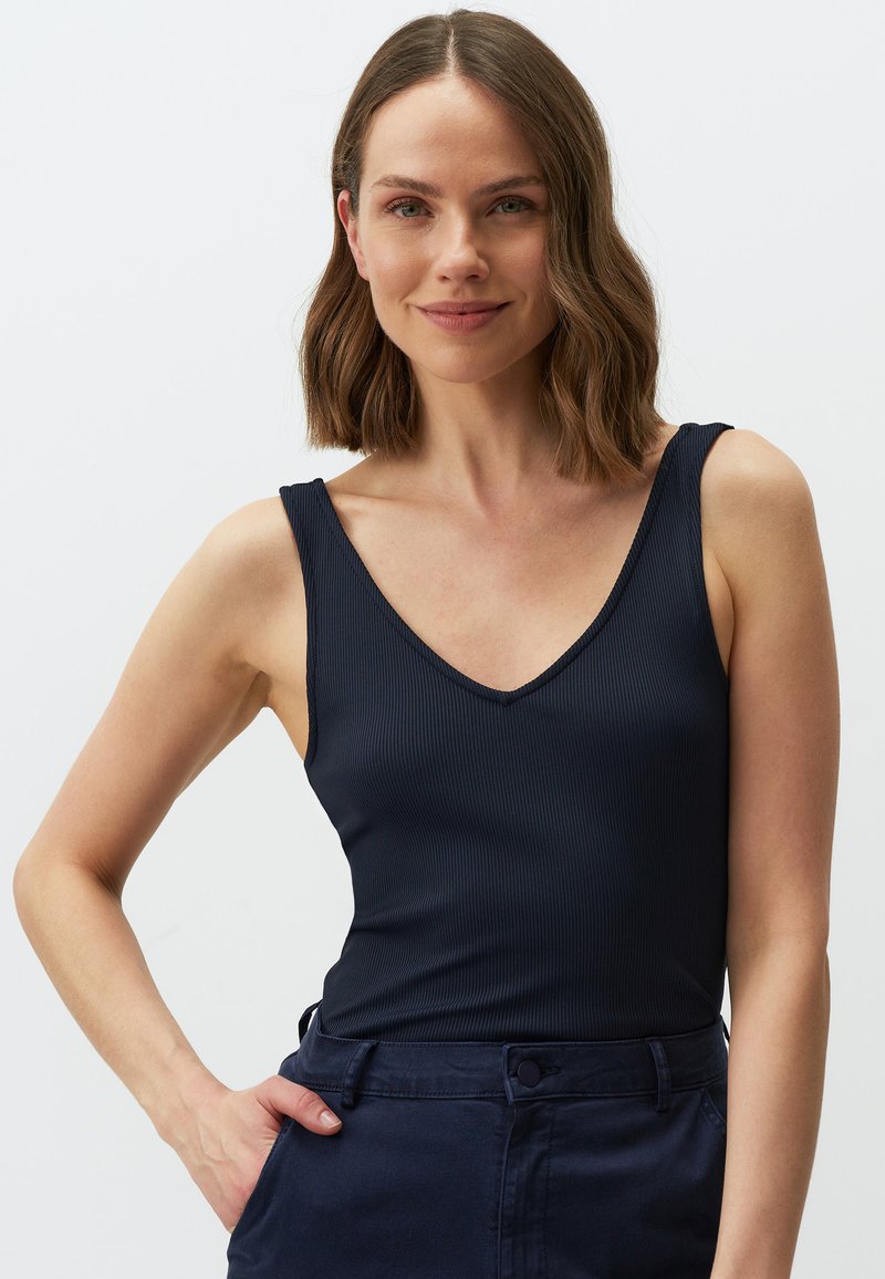 Canottiera a costine navy con spalline larghe e scollatura a V profonda, abbinata a pantaloni scuri. Tessuto liscio, design aderente, nessun motivo visibile.