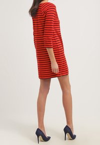 Robe rayée rouge et noire avec des manches trois-quarts, un encolure arrondie et une légère fente à l'arrière, accompagnée de chaussures à talons hauts navy.