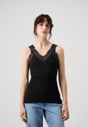 Zwarte geribde tanktop met ingewikkelde zwarte kantafwerking rond een V-halslijn en een golvende zoom. Gecombineerd met lichtblauwe denim jeans.