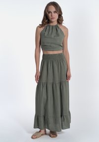 Completo a due pezzi verde oliva che presenta un top crop con scollatura all'americana e una lunga gonna a strati, realizzato in tessuto leggero con una vestibilità comoda.