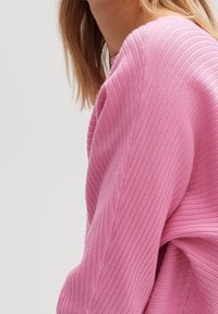 Pull côtelé rose avec un tissu texturé et doux. Conçu avec une coupe décontractée et des coutures distinctives le long des épaules.