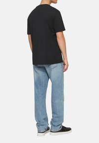 Zwarte katoenen t-shirt met korte mouwen, gecombineerd met lichtblauwe denim jeans met een relaxte pasvorm en vervaagde textuur. Zwarte sneakers maken de look compleet.