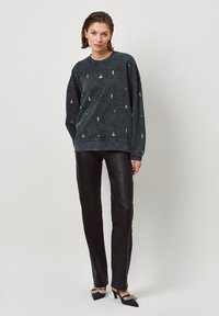Zwarte katoenen sweatshirt met subtiele bloemenborduursels, ontspannen pasvorm, gecombineerd met zwarte leren broek en versierde zwarte hakken.