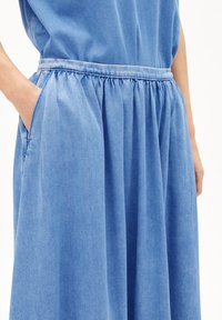 Blue denim dress featuring a gathered waist, side pockets, and a soft, lightweight texture. The fabric has a subtle, uniform pattern.