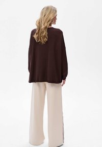 Brązowy, dziany, oversize sweter z opuszczonymi ramionami, zestawiony z kremowymi spodniami typu wide-leg z bocznymi paskami. Prosta, teksturowana tkanina.