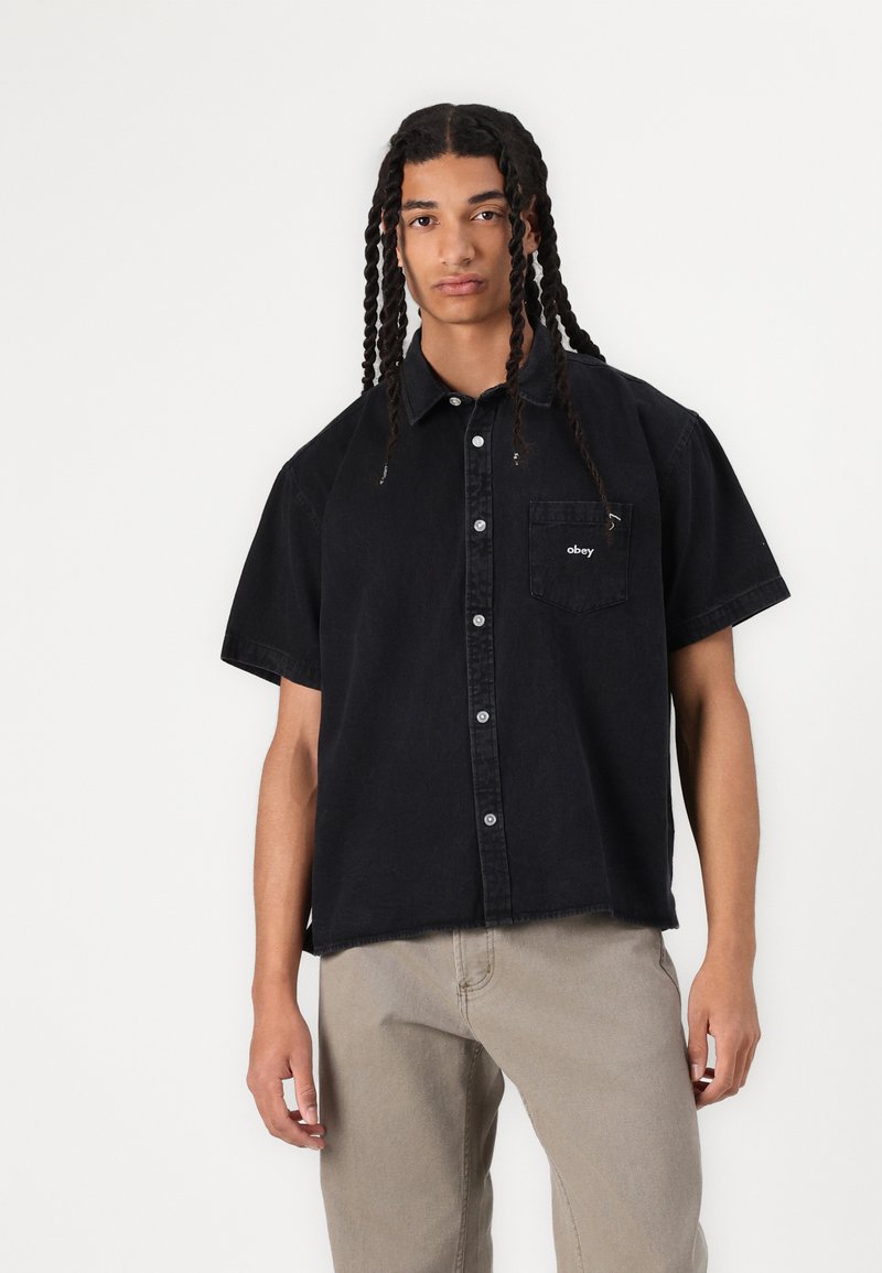 Black short-sleeve button-up shirt with a chest pocket featuring "obey" branding. Crafted from a textured fabric, designed for a relaxed fit.