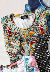 Verscheidenheid aan t-shirts die op elkaar gestapeld zijn; kenmerken omvatten kleurrijke patronen, zachte texturen, ronde halslijnen en een onderscheidend label op één shirt.