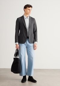 Γκρι σακάκι πάνω από ριγέ πουκάμισο, ανοιχτό μπλε τζιν παντελόνι φαρδιάς γραμμής, μαύρη τσάντα με κοντά λουριά και μαύρες μπότες. Μινιμαλιστικός σχεδιασμός.