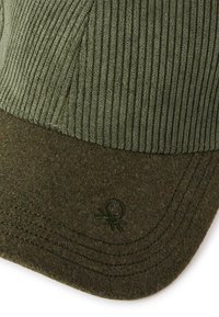 Dunkelgrüne Mütze aus Cord und Filz, mit gerippter Textur und gesticktem Logo auf dem Schirm. Genähte Details entlang der Kanten.