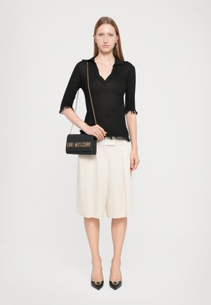 Musthave musta lühikeste varrukatega kootud tops, millel on V-kaelus ja kulunud servad, koos koorevärvi plisseeritud sortside ja mustade teravate varvastega kontsadega. Must käekott logoga.