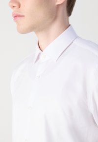 White shirt with a herringbone pattern, featuring a button-down collar and a smooth texture. The fabric appears lightweight and crisp.