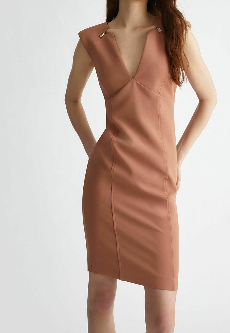 Robe ajustée sans manches en terracotta foncé. Présente un décolleté en V profond et deux accents métalliques aux épaules. Tissu lisse et texturé.