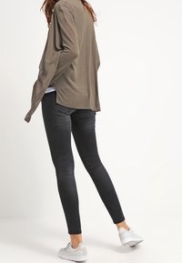 Svarta snäva jeans i kombination med en taupefärgad cardigan. Outfitten fulländas med vita sneakers med en strukturerad design.