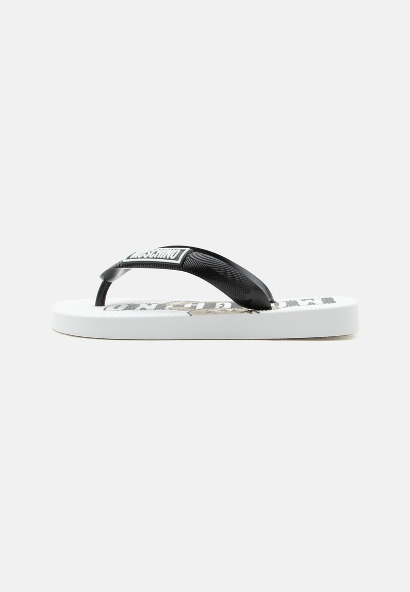 Λευκό σαγιονάρες με μαύρα υφασμάτινα λουριά που έχουν το λογότυπο της μάρκας στο πάνω μέρος, σε απλό λευκό φόντο.