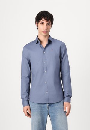 Langärmliges Hemd aus dunkelblauer Baumwolle, mit Button-Down-Kragen, Vorderknöpfen und dezentem Logo auf der linken Brust, kombiniert mit hellblauen Jeans.