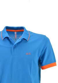 Polo blu con accenti arancioni sul colletto e sulle maniche. Presenta una chiusura a due bottoni e un logo sul lato sinistro del petto. Tessuto morbido.