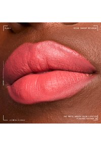 Gros plan de lèvres à la peau foncée portant un rouge à lèvres rose mat vif, montrant une texture lisse et des lignes naturelles des lèvres sans retouche de maquillage.