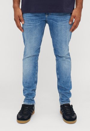 Light blue denim jeans with a slim fit, featuring a faded texture, five-pocket design, and paired with black sneakers on a white background.