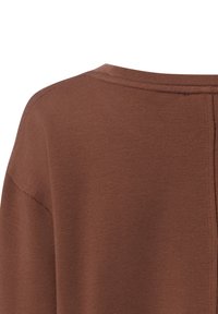 Brązowy dzianinowy top z zaokrąglonym dekoltem i krótkimi rękawami. Tkanina ma miękką teksturę z widocznymi detalami szwów.